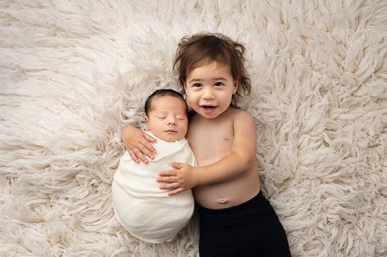 Two young siblings playfully lying together at Newborn Photography Experience