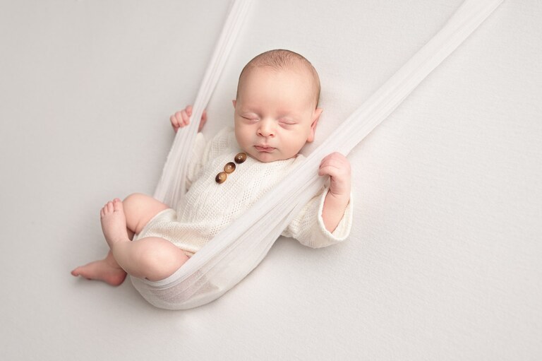 Newborn baby in a cream romper resting in a soft fabric hammock, luxury newborn session in Brooklyn