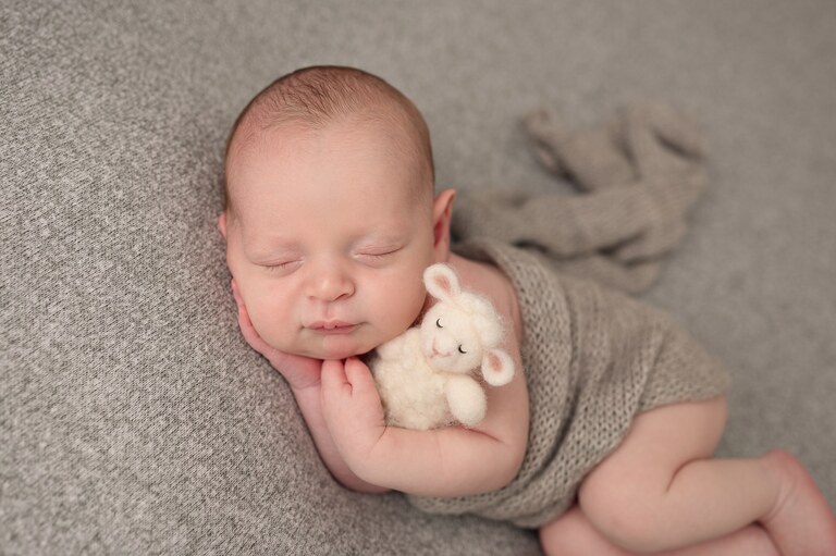 Sleeping newborn in a gray knit romper cuddling a little lamb prop, newborn photography in Brooklyn, NYC